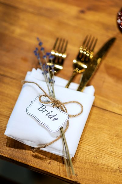 A twine-tied tag and gold cutlery wait on a folded napkin at one place setting.