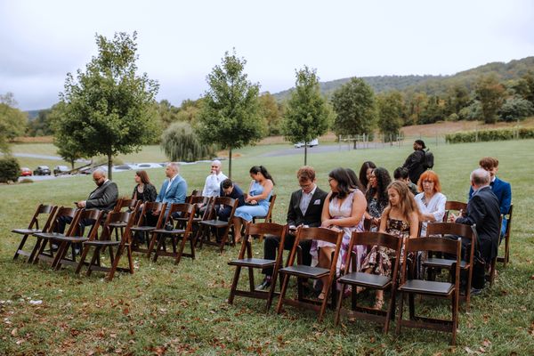 Guests settle into rows of wooden chairs as the field fills for the ceremony.