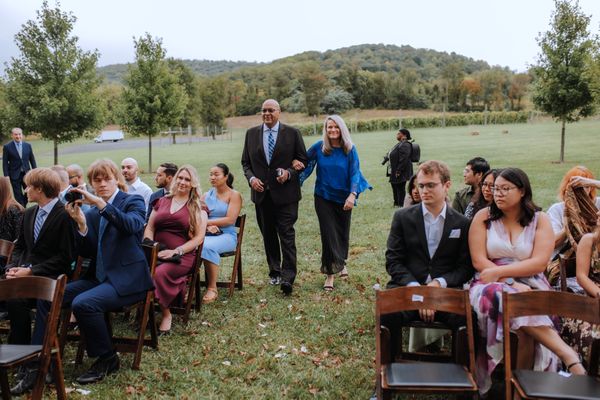 A man and a woman in blue lead the procession down the grassy aisle.