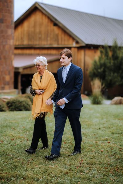 Brian walks a woman in a mustard coat across the lawn, the old barn behind them.