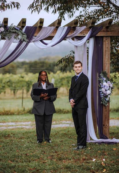Brian and the officiant wait beneath the draped arch.