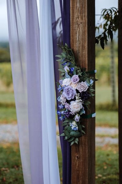 Lavender and white blooms crown a post of the wedding arch.