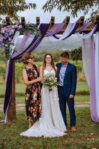Anastasia between a woman in a floral dress and a man in a blue suit.