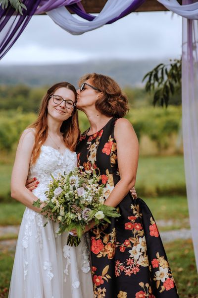 A woman in a floral dress plants a kiss on Anastasia's cheek.