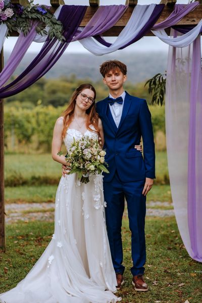 The bride and a young man in a blue suit, side by side beneath the arch.