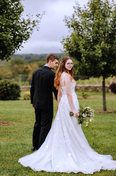 Seen from behind, the newlyweds stand close on the lawn, the train fanned out on the grass.