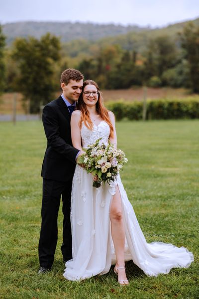 The couple stands together in the open field.