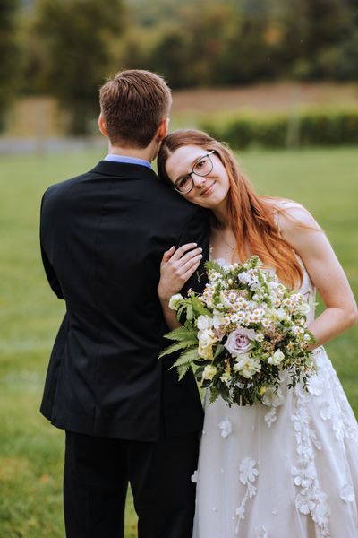 Anastasia rests her head on Brian's shoulder and smiles.
