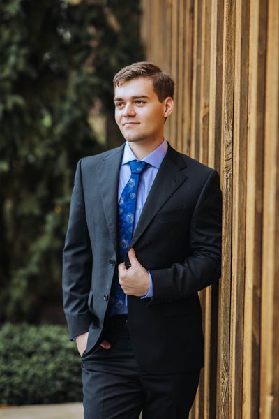 Brian leans against the wooden wall, relaxed in his suit.