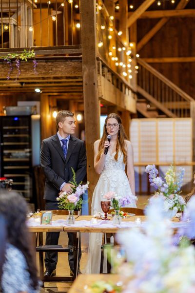 The newlyweds at the head table under the barn's string lights.