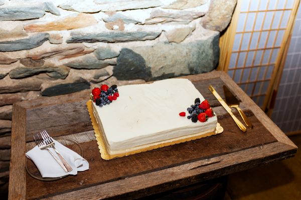 A simple white cake topped with red berries waits to be cut.