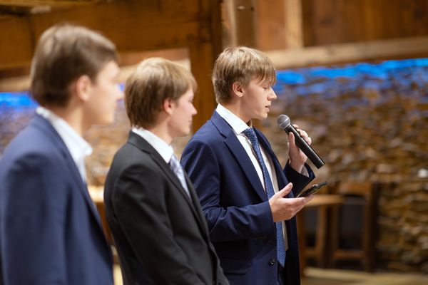 Three young men deliver a toast, one holding the microphone.