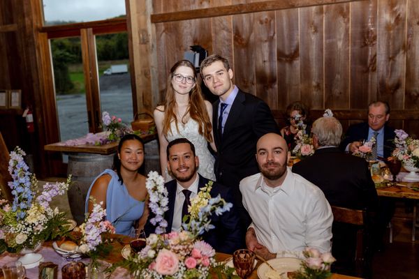 The bride and groom lean in with guests at their table.